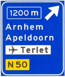 Voorwegwijzer langs autosnelweg voor de afgaande richting, met afstandaanduiding, afritnummer, interlokale doelen (bovenste doel = afritnaam), verwijzing naar vliegveld/luchthaven en routenummer niet-autosnelweg